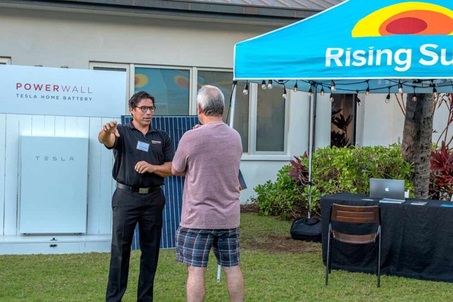 man standing in front of tesla powerwall and solar panel explaining how they work