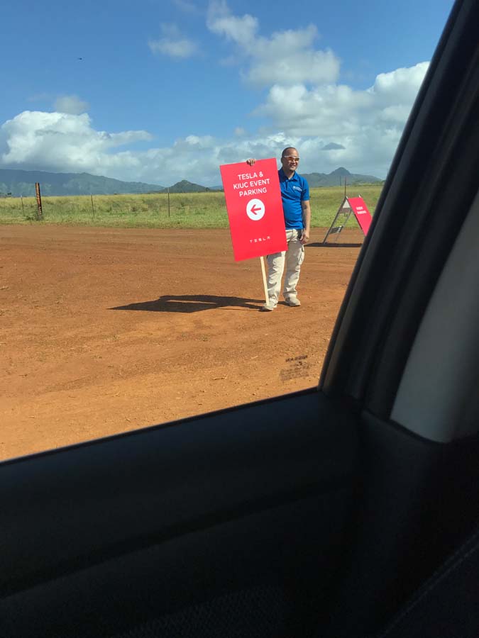 man holding a sign saying tesla & kiuc event parking