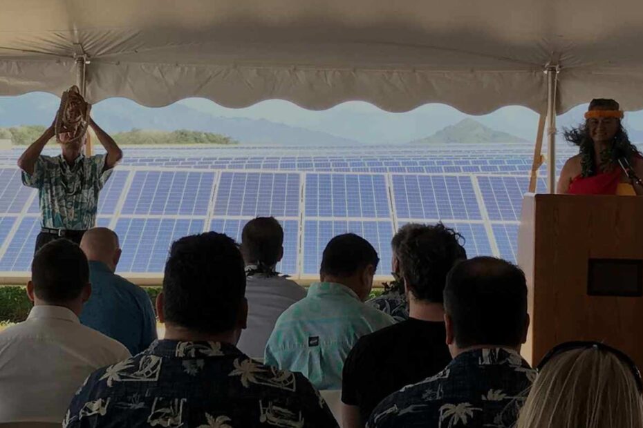 man blowing shell under a tent standing in front of a large solar array