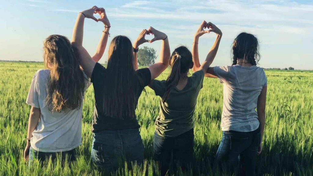 four people crossing arms over green field and blue sky