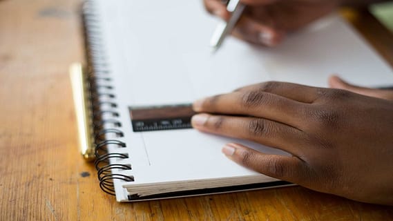 two hands writing on a notebook