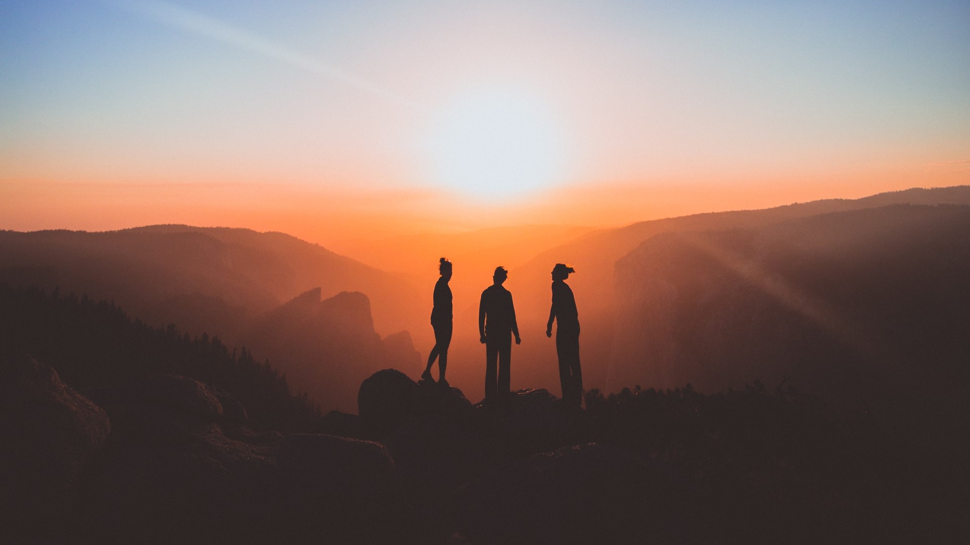 Three people watching the sun rise on a mountain top